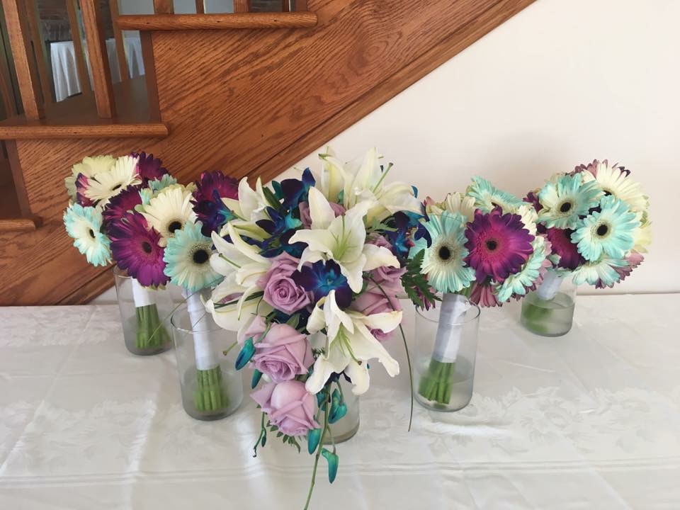 Cascade bridal bouquet of purple roses, white lilies, and teal-tipped gerbera daisies