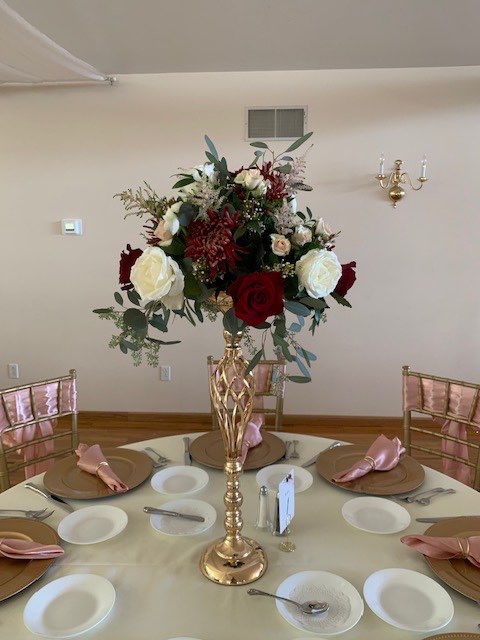 Tall centerpiece of burgundy and white roses on a gold stand